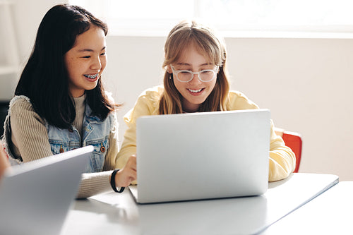 Happy female classmates doing a digital literacy task together in a classroom