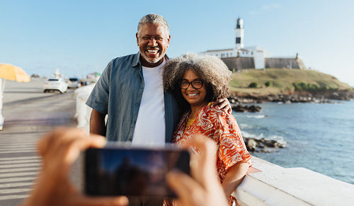Happy black couple smiling while posing for a vacation photo by the ocean