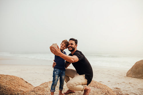 Father and son taking selfie at the rocky beach
