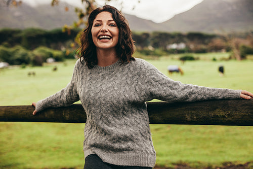 Cheerful woman leaning to a fence in countryside