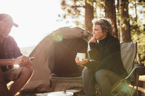 Relaxed couple sitting outside tent while camping nearby lakeside