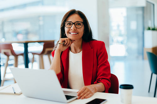 A confident businesswoman working on a laptop at a bright office desk