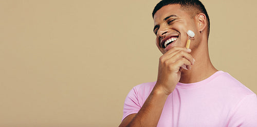 Anti-aging massage with a jade roller: Happy young man practicing his skincare routine