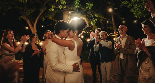 Intimate outdoor wedding celebration with guests under string lights at nighttime