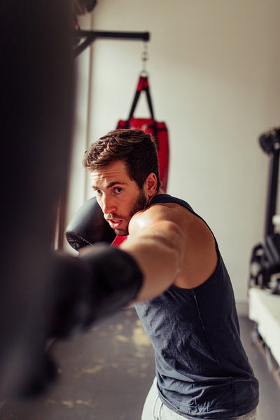 Muscular boxer striking a punching bag with one gloved fist