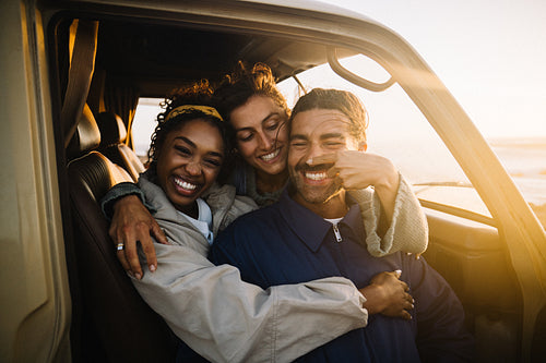 Three friends share a playful sunset moment in a car