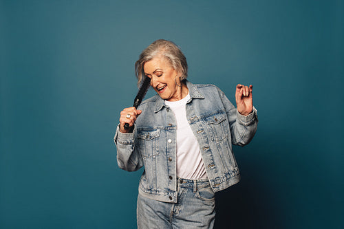 Happy older woman dancing and singing to music in studio with blue background