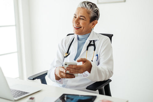 Medicine with technology: Happy female doctor holding a smartphone in her office