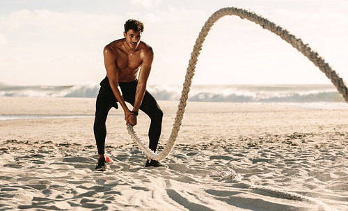 Man doing fitness training at the beach using battling rope