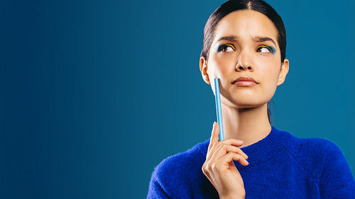 Pensive over her new makeup look, woman looks away holding an eyeliner pen