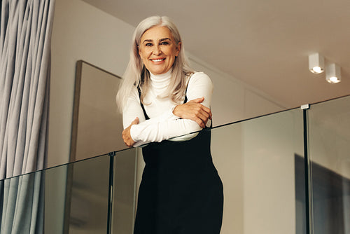 Silver-haired senior woman smiling as she stands on a balcony at home