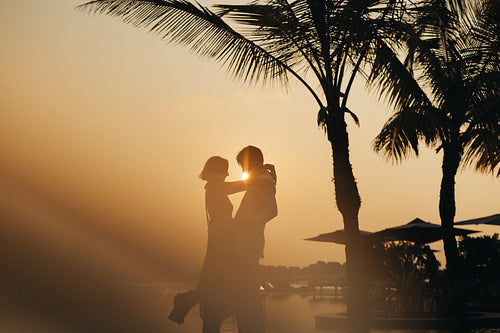 Romantic couple dancing by the ocean at sunset under palm trees