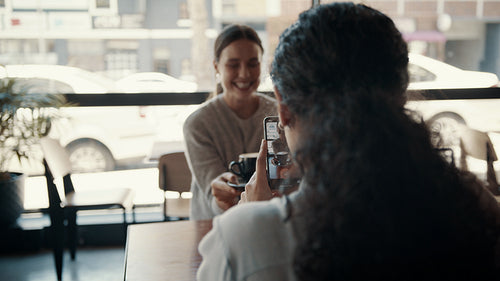 Woman photographing her friend holding a coffee at a cafe