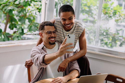 Couple smiling together taking a selfie at home surrounded by bright daylight