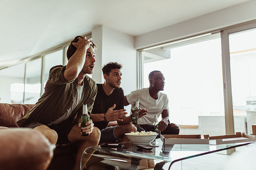 Three male friends sitting in suspense watching a game on TV