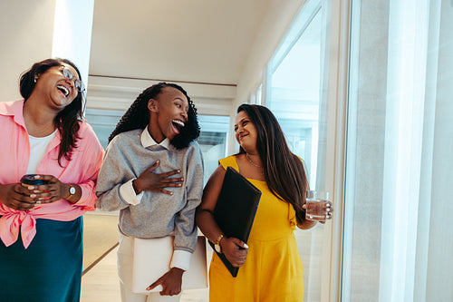 Three colleagues sharing a laugh on a relaxed Friday afternoon while walking through the office corridor