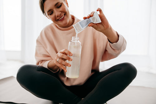 Woman mixing electrolytes into water for hydration post workout