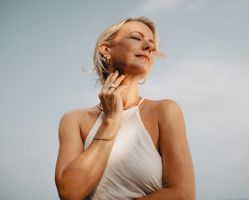 Elegant woman wearing luxurious gold jewelry with serene outdoor background