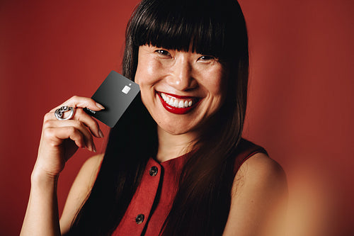 Smiling woman uses a black credit card in a studio portrait for consumer finance