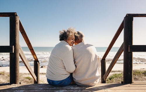 Senior woman smiling while sitting with her husband at the beach