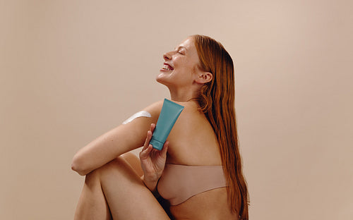 Smiling woman holding skincare tube and applying lotion
