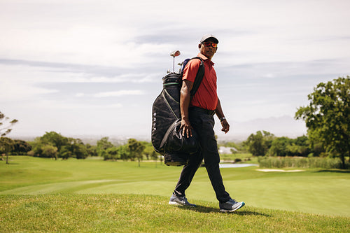 Pro golfer walking on golf course while carrying a golf bag on a fun day playing sport.