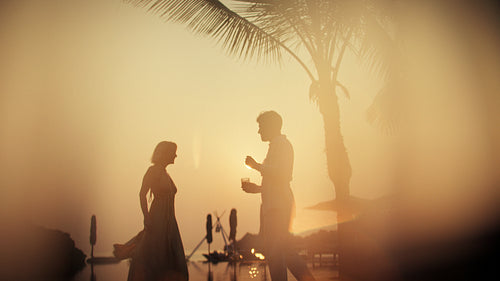 Honeymoon couple enjoying cocktails at a tropical sunset by the resort pool