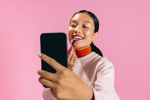 Gen Z female using a smartphone to apply lipstick in a studio