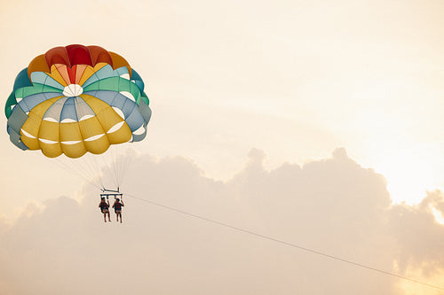 Two people parasailing at sunset with colorful parachute against a serene sky