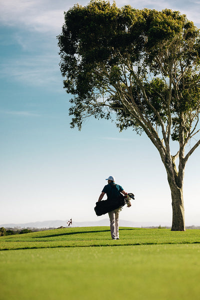 Man carrying golf bag along the fairway of a scenic golf course on a crisp spring morning
