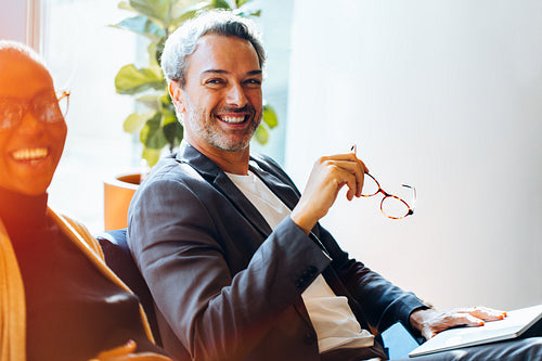 Smiling man in a meeting with a colleague holding his glasses