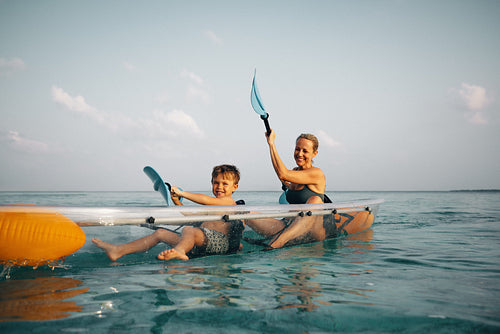 Smiling parent and child rowing a transparent boat on the sea