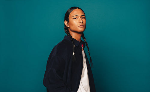 Confident Native American man with braided hair standing against blue background