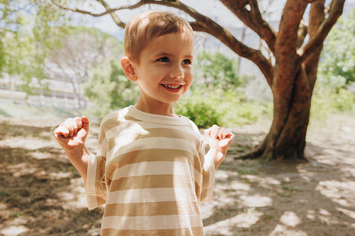 Cheerful young boy smiling outdoors under trees on a sunny day
