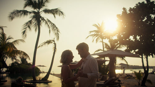 Romantic couple dancing at sunset on a tropical beach vacation with palm trees