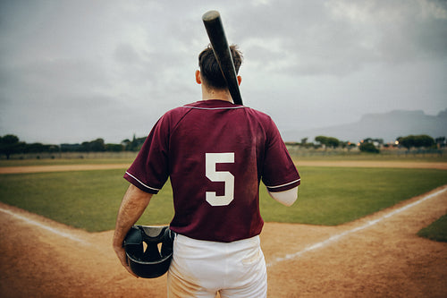 Baseball player in maroon jersey number 5 stands ready with bat on shoulder