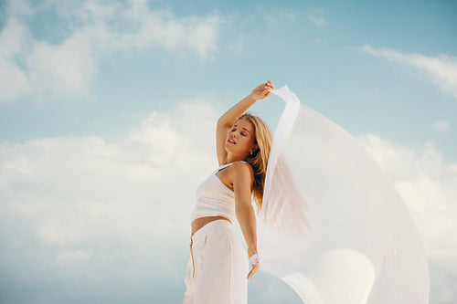 Young woman posing gracefully outdoors with white fabric under a bright sky