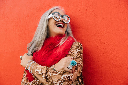 Cheerful senior woman laughing happily against a red wall