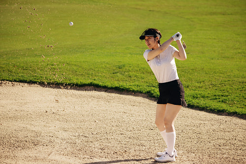 Asian female golfer taking a shot from sand bunker with perfect swing on golf course