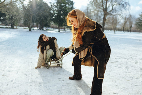 Woman pulls friend on a sled through snowy park