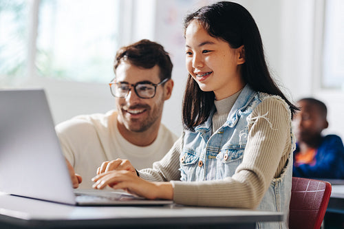 Teacher assisting a young girl in a computer science class