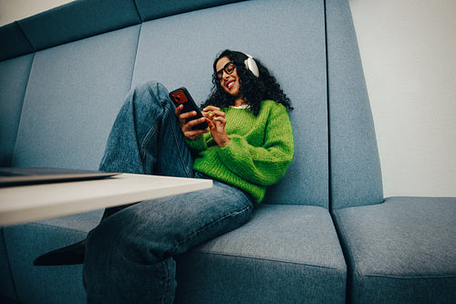 Woman relaxing with smartphone and headphones in study lounge
