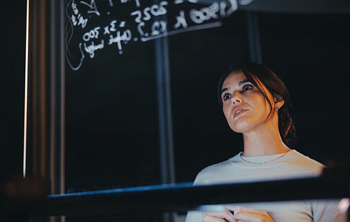 Female entrepreneur and data analyst brainstorming in a glass-walled office at night