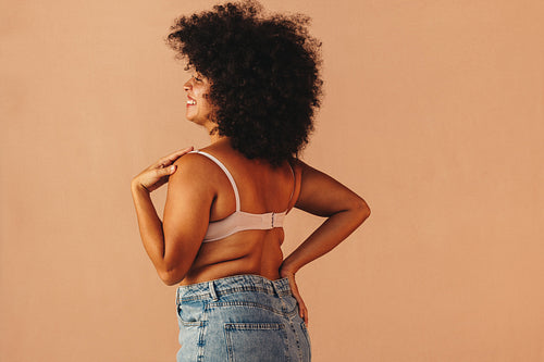 Self-confident woman smiling while wearing a bra and jeans