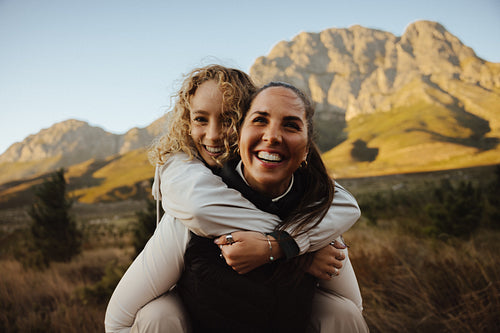 Woman piggybacking friend in mountain landscape