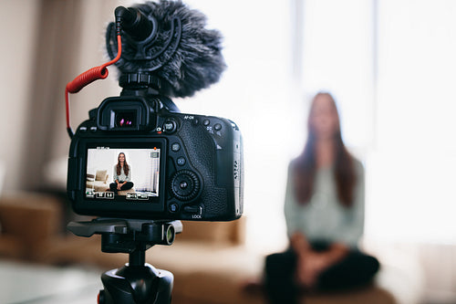 Young woman recording daily video blog on camera mounted on tripod.