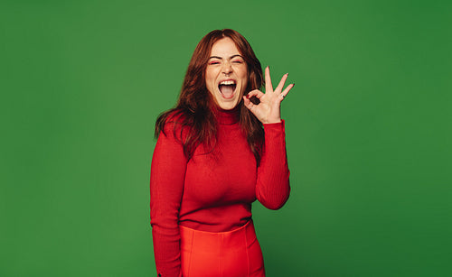 Vibrant woman excitedly flaunts ok gesture in trendy green studio setting
