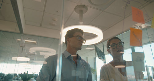 Business people discussing over adhesive notes on glass wall