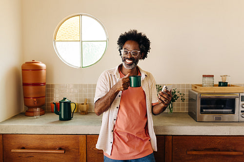 Mature afro-brazilian man smiling in kitchen with enamel mug