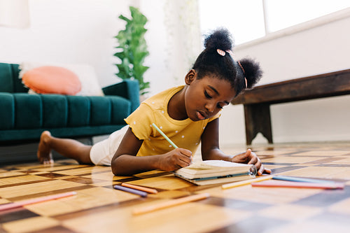 Creative afro-haired girl drawing in a colouring book at home